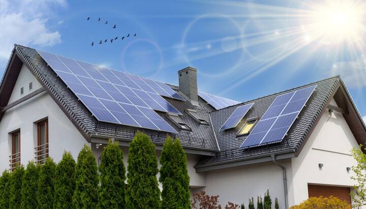 A close-up view of a residential rooftop solar panel installation in Modesto, CA. The solar panels are arranged in a neat pattern and angled towards the sun to capture the maximum amount of energy. The roof of the house is visible in the background, with clear blue skies and a few clouds.