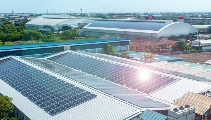 A commercial office building with solar panel installation on its rooftop in Modesto, CA. The solar panels are positioned to capture maximum sunlight, with the city skyline visible in the background. The installation team can be seen working on the rooftop, arranging the panels and connecting them to the building's electrical system. The sky is cloudy with a hint of sunlight breaking through.